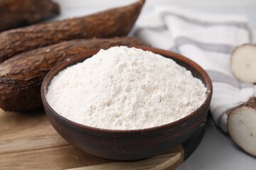 Bowl with cassava flour and roots on white table, closeup