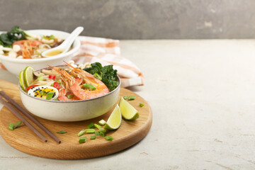 Delicious ramen with shrimps, egg in bowl and chopsticks on light textured table, space for text. Noodle soup