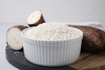 Tapioca pearls in bowl and cassava roots on table, closeup