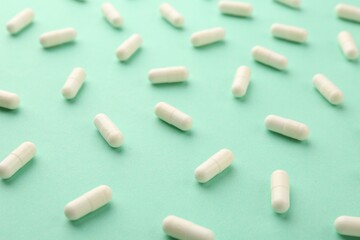 Many vitamin capsules on turquoise background, closeup