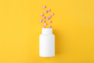Bottle and vitamin pills on yellow background, top view