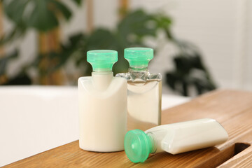 Wooden tray with mini bottles of cosmetic products on bath tub in bathroom