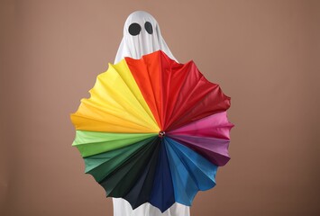Person in ghost costume with rainbow umbrella on dark beige background