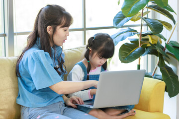 Asian young mother and her little cute daughter girl learning study from laptop computer, sitting...