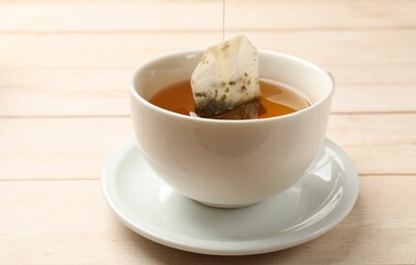 Putting tea bag in cup on light wooden table, closeup