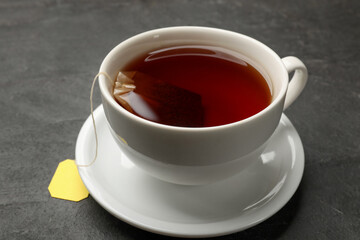 Tea bag in cup with hot drink on grey textured table, closeup