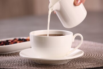 Woman pouring milk into cup with aromatic tea at table, closeup