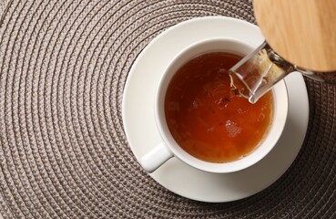 Pouring aromatic tea into cup at table, top view. Space for text