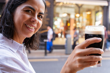 Latin woman looking towards the camera with a Guinness toasting with her companion while enjoying a...