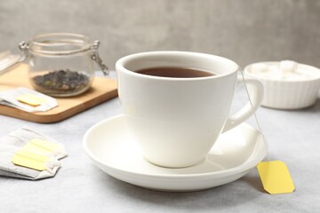 Obraz na płótnie Canvas Tea brewing. Cup with hot drink and tea bags on light table, closeup