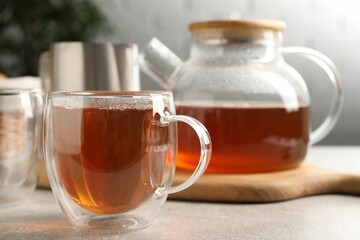Aromatic tea in glass cup and teapot on light grey table