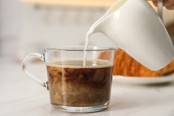 Pouring milk in coffee at white table, closeup