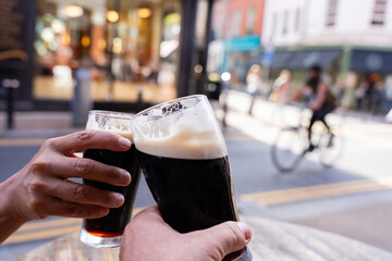 Close-up of two hands toasting each other with Guinness beers on a central Dublin street having a good time on a beautiful autumn morning - obrazy, fototapety, plakaty