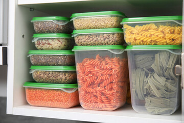 Plastic containers filled with food products in kitchen cabinet, closeup
