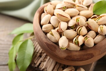 Delicious pistachios in bowl on wooden table, closeup