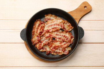Delicious bacon slices in frying pan on white wooden table, top view