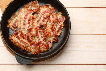 Delicious bacon slices in frying pan on white wooden table, top view. Space for text