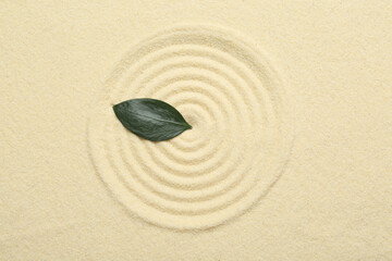Zen rock garden. Circle pattern and green leaf on beige sand, top view