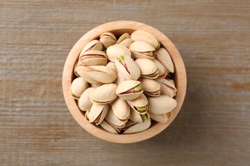 Tasty pistachios in bowl on wooden table, top view