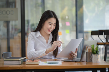 Happy asian young businesswoman holding documents folders in office working space, Asian female employee using laptop talking on the phone at workplace.