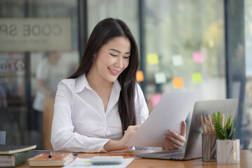 Happy asian young businesswoman holding documents folders in office working space, Asian female employee using laptop talking on the phone at workplace. - obrazy, fototapety, plakaty