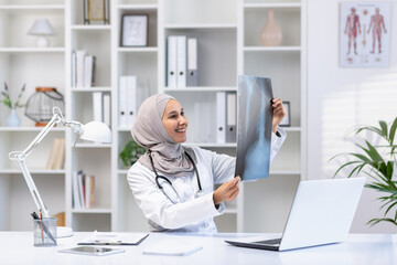 Smiling Muslim female doctor in hijab reviewing an X-ray in a well-lit medical office, reflecting...