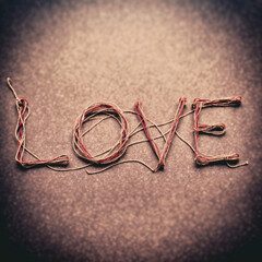 The word love is written in red and gray threads on a brown board background.