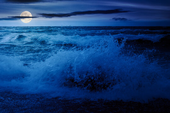 waves crashing the shore at night. stormy seascape in full moon light