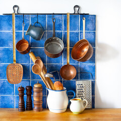 Kitchen interior with vintage copper utensils. old style cookware kitchenware set. Pots, spoons, grater, skimmer hanging on blue tile wall. - 734854582
