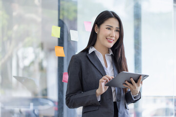 Fototapeta premium Happy asian young businesswoman using digital tablet standing in office office working space.