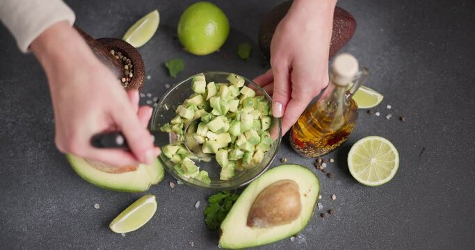 Woman mixing Sliced chopped avocado fruit with lime juice and species in a glass bowl at domestic kitchen