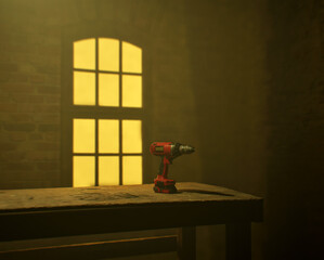 Red electric drill on an old wooden table by a lit window in an dusty workshop.