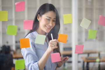 Startup successful asian businesswoman working with sticky note on glass wall and meeting to share idea at office, Business planning and Sticky note on glass wall to share idea, successful creative.