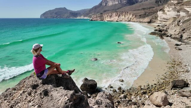 A tourist woman discovers the hidden beach of Al Fizayah in Salalah, Oman. Pristine white sands meet crystal-clear waters, framed by the awe-inspiring coast of Salalah city of south Oman.