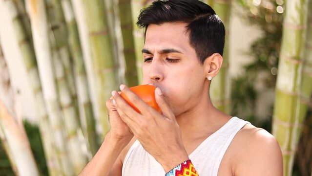 Latino beardless man blowing up an orange balloon with mouth in street