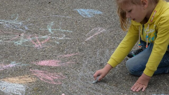 Child paints outdoors. Little girl drawing colored chalk on the asphalt . Creative development of children