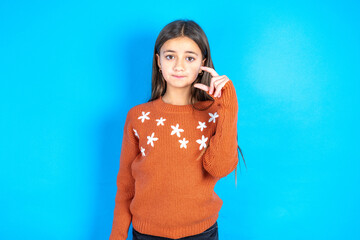 Young beautiful teen girl wearing orange knitted sweater purses lip and gestures with hand, shows something very little.