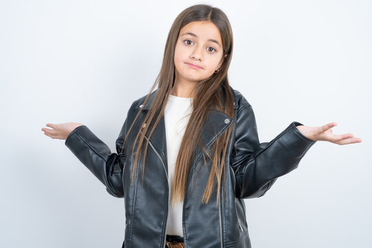 Careless attractive Young beautiful teen girl wearing biker jacket shrugging shoulders, oops.