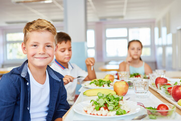 Smiling boy sitting with food plate on table in school cafe