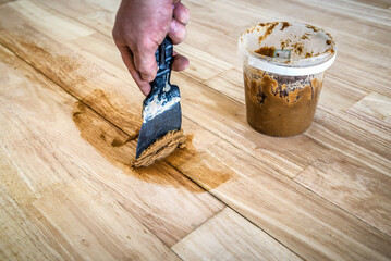Carpenter fills the gaps cracks in the parquet with a spatula. Mixing retainer, varnish and a small...