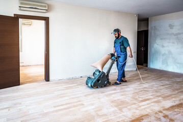 Professional carpenter worker grinding sanding wooden parquet floor by using floor sander.