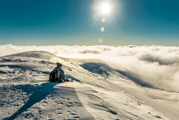 Tourist hiker sitting on the snow in winter snowy mountains under sunlight