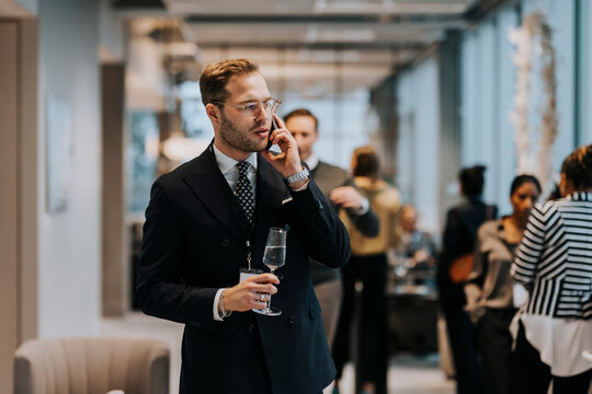 Young businessman holding champagne flute while talking on mobile phone during business conference