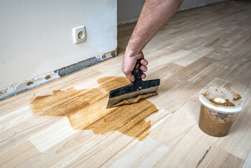Worker fills the gaps cracks of the old parquet with a spatula after sanding. Floor renovation