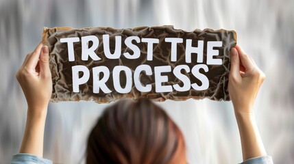 Motivated woman holding sign  trust the process  for success on blurred background