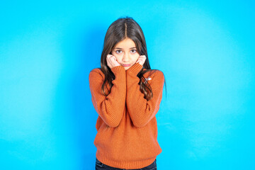 Portrait of sad beautiful kid girl wearing orange sweater hands face