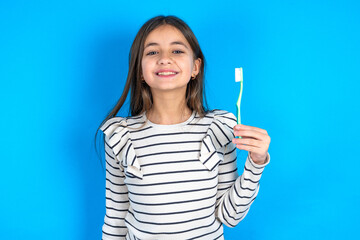 beautiful kid girl wearing  striped T-shirt holding a toothbrush and smiling. Dental healthcare concept.