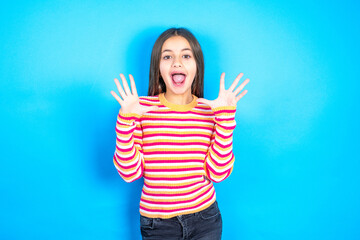 Delighted positive beautiful kid girl wearing  striped T-shirt opens mouth  and arms palms up after...