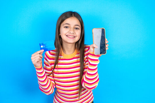 Young kid girl wearing striped t-shirt opened bank account, holding smartphone and credit card, smiling, recommend use online shopping application