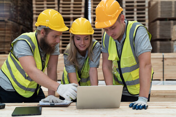 Male and female warehouse worker working with laptop computer in lumber storage warehouse. Workers...